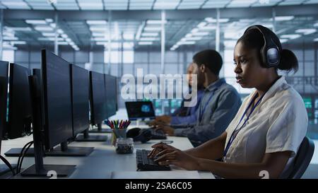 Portrait of smiling engineer hearing podcasts to make time pass faster while working in server farm to optimize it for data processing requirements. Happy woman listens songs in data center, camera A Stock Photo