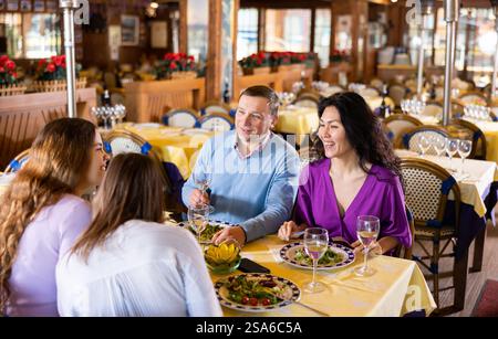 Man and woman chatting with female friends while having dinner in restaurant Stock Photo