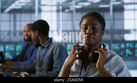 Portrait of smiling engineer hearing podcasts to make time pass faster while working in server farm to optimize it for data processing requirements. Happy woman listens songs in data center, camera A Stock Photo