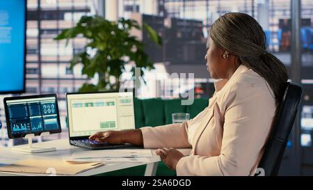 Black influential businesswoman evaluates company performance, using data reports and analytics to make informed decisions that optimize efficiency and productivity. Work ethic. Camera A. Stock Photo