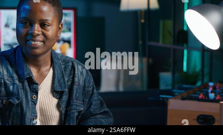 Jolly freelancer noting down ideas on paper using pen while teleworking. Upbeat remote employee working at home office desk, reading information on laptop and writing in notebook, camera A Stock Photo