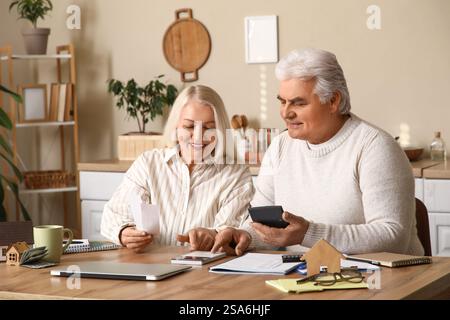 Happy senior couple calculating utility bills at table in kitchen Stock Photo