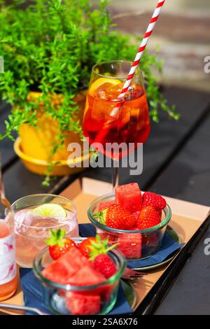 A vibrant scene with chilled summer drinks, one garnished with lime and another in a wine glass with a striped straw, alongside bowls of fresh strawbe Stock Photo
