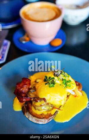 Classic Eggs Benedict with poached eggs, crispy bacon, hollandaise sauce and microgreens garnish, served on toasted sourdough bread. Stock Photo