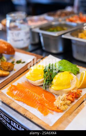 Poached eggs on English muffins topped with hollandaise sauce, served with smoked salmon, avocado, and fresh arugula on wooden board. Stock Photo