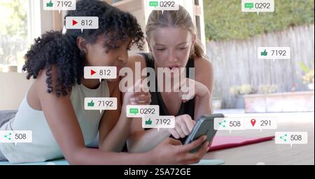 Image of social media text and icons over diverse girlfriends using smartphone Stock Photo