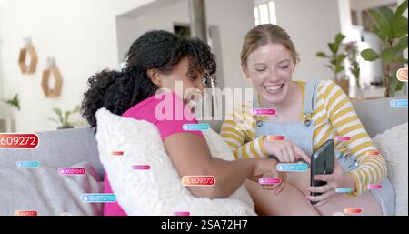 Image of social media text and icons over diverse girlfriends using smartphone Stock Photo