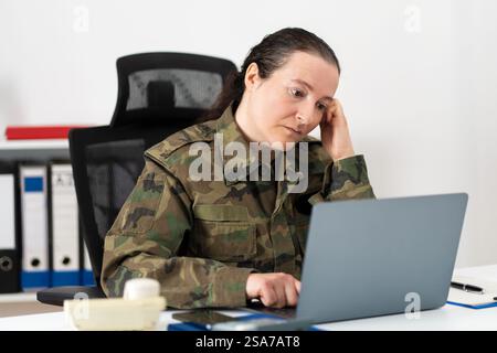 Female soldier with a stress headache feeling tired, pain and stressed while working on a computer.Unhealthy female soldier with stomach ache with her Stock Photo