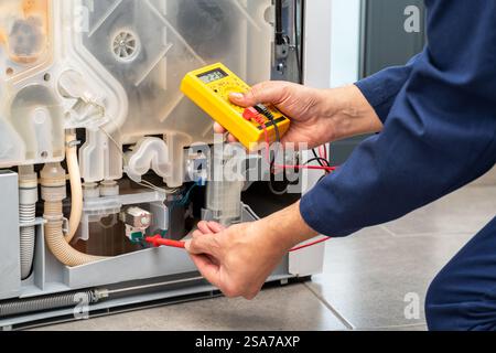 Shot of a young man using an electronic multimeter while repairing a dishwasher in a house Stock Photo
