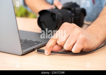 Close-up of a man's hand plugging a usb cable into a laptop from a camera at home Stock Photo