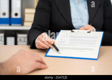 Close up of an executive hands holding a pen and indicating where to sign a contract at office Stock Photo