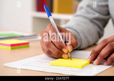 Close up of black man hand writing reminder on sticky note on a desk at home Stock Photo