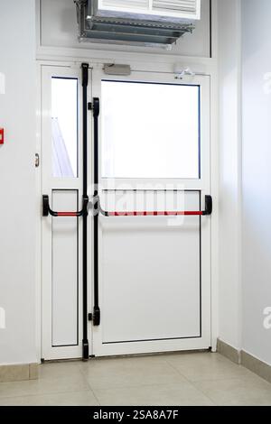 Modern double door with red safety bar in a clean, well-lit hallway of a building Stock Photo