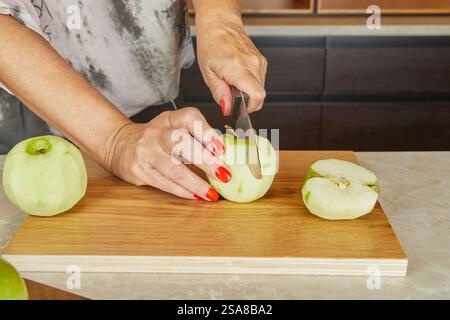 A person slices a peeled green apple on a wooden cutting board. The apple is cut into halves and quarters in preparation for baking. Stock Photo
