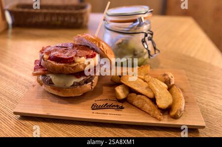 A unique "pizza" burger and fries made by the restaurant Builders in Tokyo, served on a wooden platter and with a jar of pickles visible behind Stock Photo