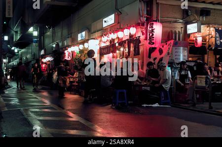 Colorfully-lit night view of a number of customers eating and drinking at a bar-restaurant located underneath elevated train tracks in west Tokyo Stock Photo