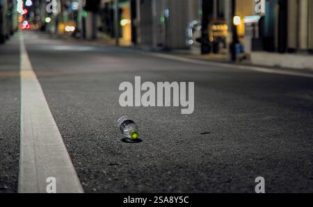 A single discarded plastic bottle lying on an empty street at night in a quiet area of Tokyo, Japan Stock Photo