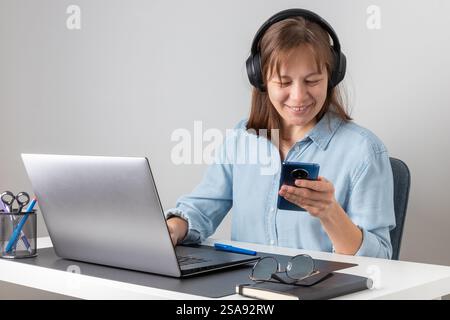 Young happy freelancer, smiling pretty professional businesswoman worker looking at smartphone, using cellphone mobile technology working at home or i Stock Photo