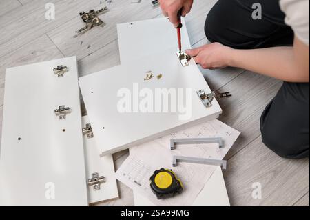 Furniture assembly. A worker is screwing a hinge into a wooden closet door. Adjustment of fittings, door hinges. The concept of installing furniture, Stock Photo