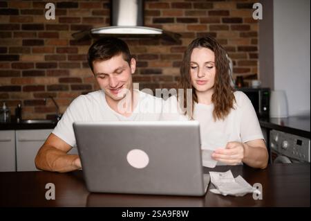 Young married couple checking expenses, bookkeeping, bills, sitting at kitchen, happy with debt repayment. Couple planning family budget, feeling sati Stock Photo