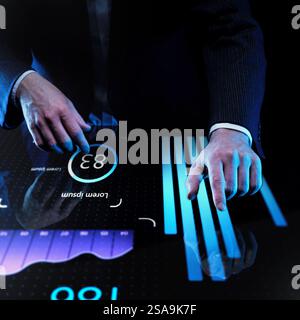 Businessman in dark suit interacting with futuristic touch screen displaying glowing blue bar charts and circular data interface against dark Stock Photo