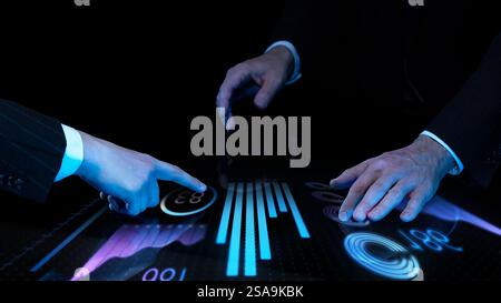 Two business professionals analyzing digital financial data on interactive touch screen with futuristic glowing blue graphs against dark background. Stock Photo