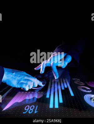 Two professionals engaging with futuristic digital interface, interacting with glowing blue data visualization, analytics, and bar charts against dark Stock Photo