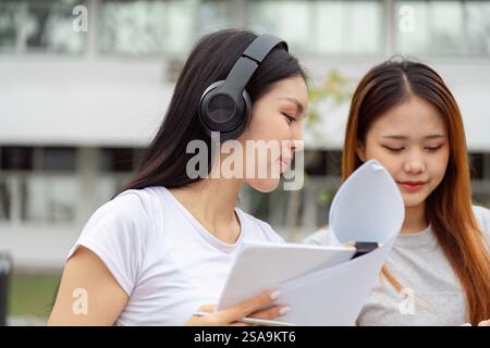Focused students collaborating with headphones and study materials outdoors Stock Photo