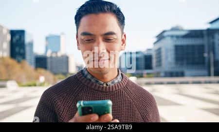 Young Man Smiling While Using Smartphone Outdoors in the City Stock Photo