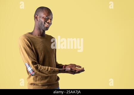 African American Man holding empty space with hands on a yellow background, ideal for marketing, product placement, and creative design templates. Stock Photo