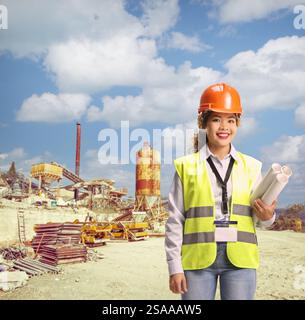 Asian female engineer in a reflective vests holding blueprints at a construction site Stock Photo