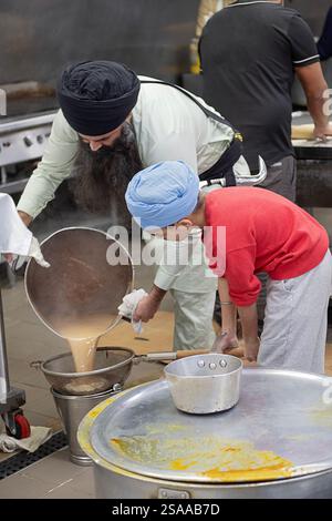 A Sikh priest with the help of his son strains soup to be offered in the temple's langar where everyone is offered a free meal. In Queens, New York. Stock Photo