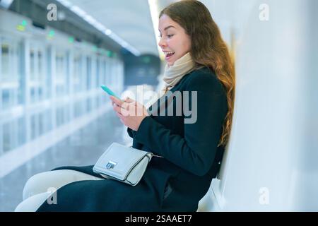 Young Woman Smiling While Using Smartphone in Modern Subway Station Stock Photo