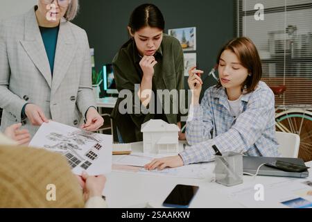 Group of diverse architects collaborating on urban model design in modern office environment, surrounded by design tools and model. Engaging in animated discussion and planning Stock Photo