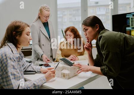 Group of diverse colleagues engaging in collaborative discussion around office table with various devices. Bright office space with large windows and city view in background Stock Photo