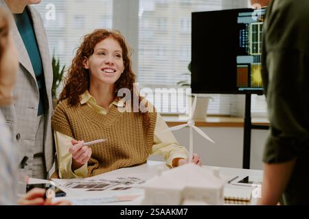 Group of professionals engaged in discussions around design and architectural models. Focus on young woman holding a pen, engaging with colleagues Stock Photo
