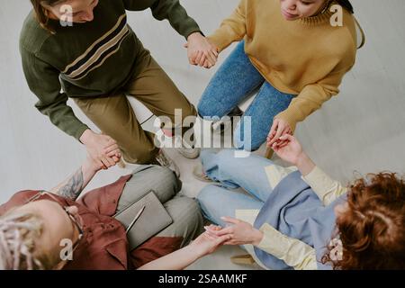 Top view of diverse people sitting on floor holding hands in circle creating connection and unity during group activity Stock Photo