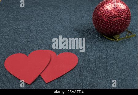 Two red hearts and Christmas New Year bauble on black background textured. Beautiful copy space. Stock Photo