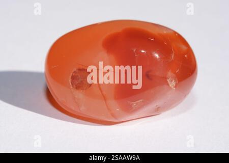Close-up of a vibrant carnelian mineral stone against a white background, showcasing its rich red-orange hues and smooth texture in detail Stock Photo