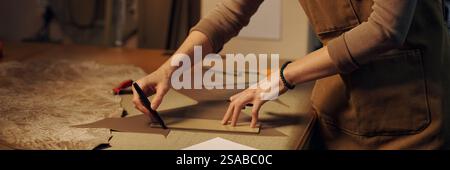 Person carefully measuring and cutting material on workbench. Workspace filled with tools and materials, indicating a focus on precision and attention to detail Stock Photo