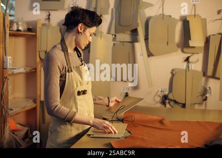 Person focusing on crafting leather accessories standing in a workshop filled with patterns and tools. Creating handmade leather goods Stock Photo