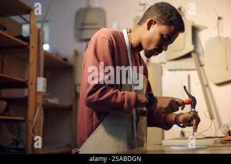 Person focused on woodworking task in a well-equipped studio with various tools hanging on walls. Careful craftsmanship is being displayed for creating precise results Stock Photo