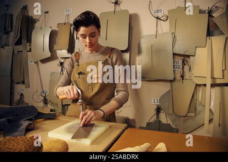 Woman concentrating on creating fashion patterns in atelier setting surrounded by various templates and tools hanging on walls Stock Photo