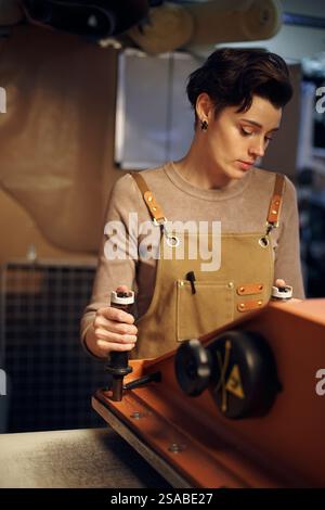 Individual intently working in a workshop while wearing an apron and using machinery. Concentrated and attentive, performing a manual task with precision Stock Photo