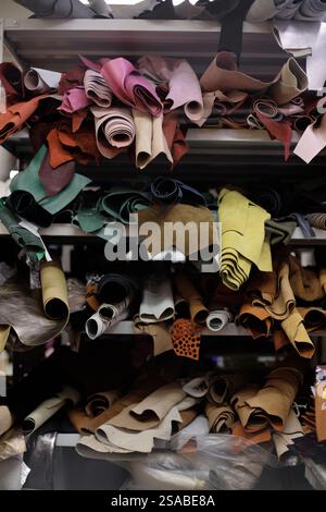 Various rolls of leather in different shades and textures are placed on metal storage shelves creating an organized yet random appearance Stock Photo