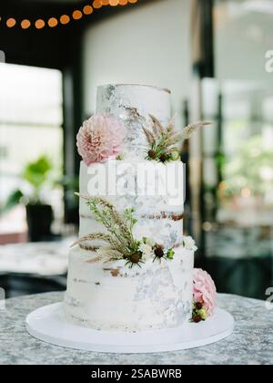 A stunning three-tier wedding cake features elegant white frosting, delicate flowers, and greenery, all displayed beautifully in a charming, romantic Stock Photo