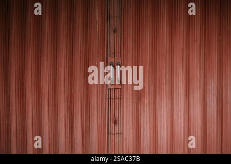 Close-up of a weathered red rolling shutter door with metal handles, adding a vintage industrial touch. Stock Photo