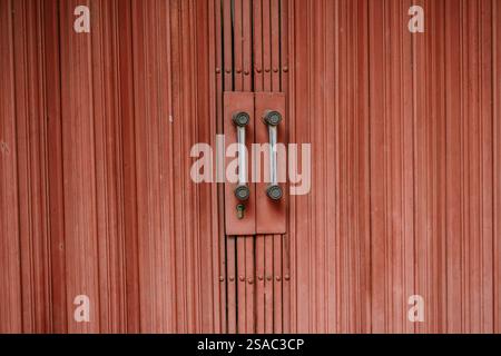 Close-up of a weathered red rolling shutter door with metal handles, adding a vintage industrial touch. Stock Photo