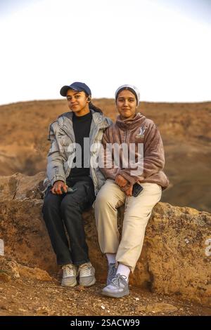 2 young women sitting on rock and smiling at the camera, Tazert, Morocco Stock Photo