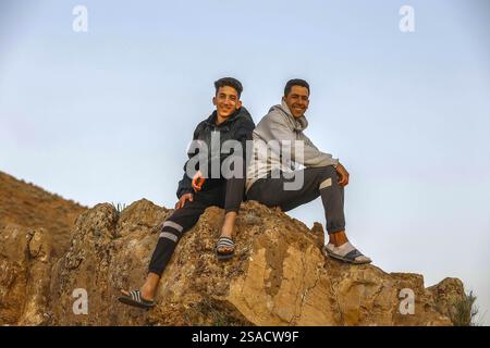 2 young men sitting on rock and smiling at the camera, Tazert, Morocco Stock Photo